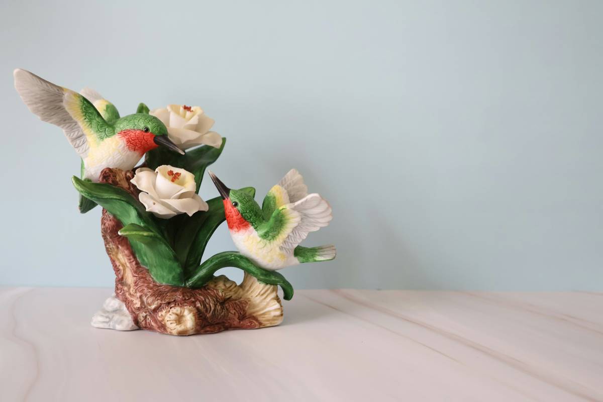 A curated shelf display featuring bird figurines home decor in ceramic, metal, and glass finishes arranged with books and greenery